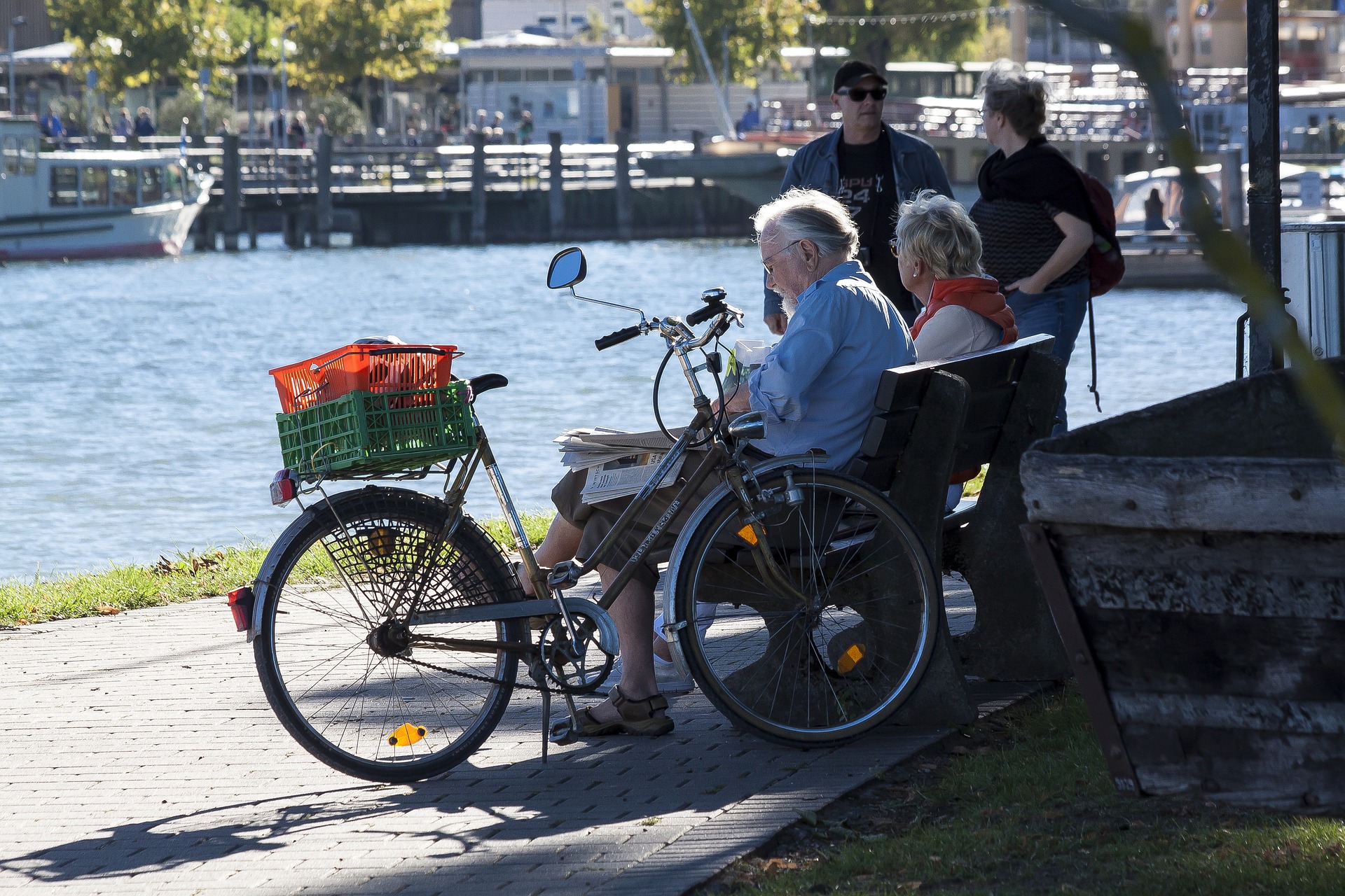 senior man and woman sitting on a bench at the waterfront with a bicycle beside them
